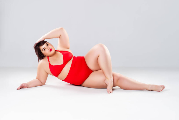 Plus size fashion model in red swimsuit, fat woman in lingerie on gray background, body positive concept - 写真・画像
