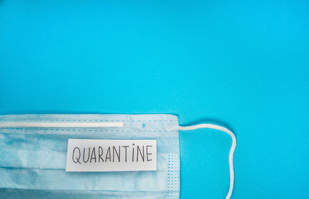 Medical mask and text QUARANTINE on a blue background, top view with a copy of the space. Quarantine, incubation period of the disease, risk of infection from infected patients - Foto, imagen