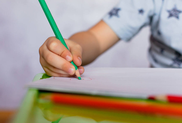 Close-up de crianças mãos desenho. O rapazinho tem lápis de cor. A desenhar um desenho para o dia dos pais. Menino pequeno desenha na mesa
. - Foto, Imagem