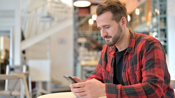 Attractive Beard Young Man using Smartphone in Cafe - Fotó, kép