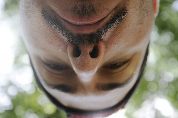 Breed hoekportret van een man. Close-up van de neus en snorren, van onderen genomen. Groene bomen en fel licht op de achtergrond. - Foto, afbeelding