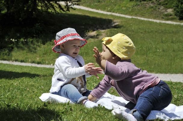 Dvě veselé kavkazské holčičky si spolu hrají v parku na trávě. Pojem mateřství, dětství, přátelství a letní prázdniny. - Fotografie, Obrázek