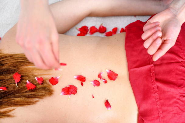 Mulher bonita recebendo massagem e tratamento de spa com pétalas de flores no salão de spa
. - Foto, Imagem