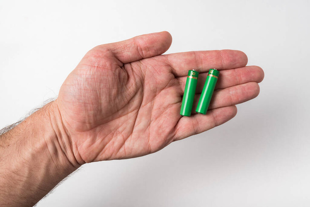 Due batterie AA sono sui palmi delle mani degli uomini su sfondo bianco. Accumulatori
 - Foto, immagini