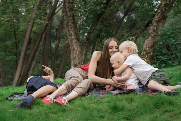 Picnic familiar en el parque Gaden al aire libre. Mamá y tres niños descansan en la manta de picnic
 - Foto, Imagen
