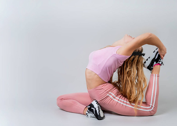 Fitness, Sport, Training und Lifestyle-Konzept. Athletische Akrobatin in pinkfarbener Sportbekleidung beim Yoga im Studio isoliert auf grauem Hintergrund - Foto, Bild