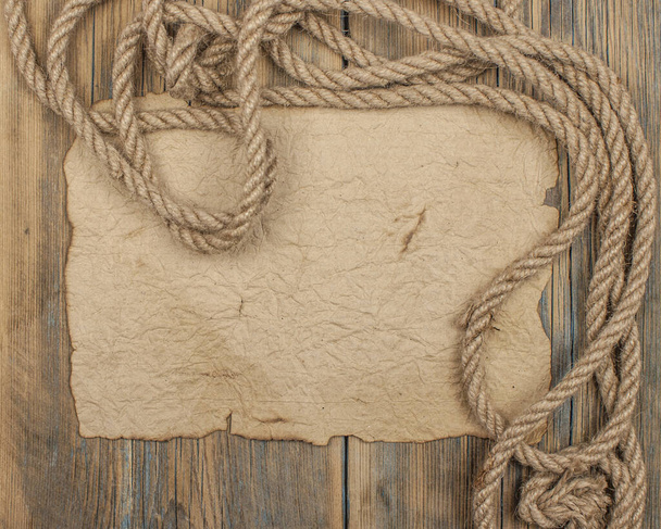 old sheet of parchment or paper lying on wooden boards and a coarse rope pulled into a nautical knot forming a frame - Photo, Image