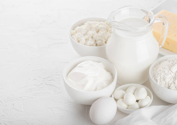 Fresh dairy products on white background. Glass jar of milk, bowl of sour cream, cottage cheese and baking flour and mozzarella. Eggs and cheese. - Photo, image