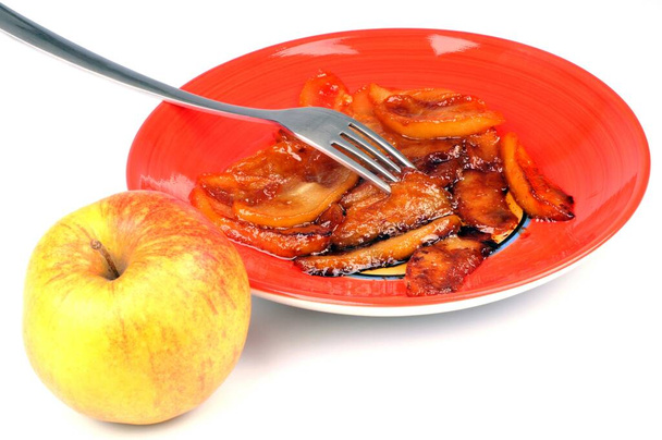 Pomme à côté d'une assiette de pommes caramélisées gros plan sur fond blanc
 - Photo, image