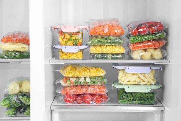 Plastic bags and containers with different frozen vegetables in refrigerator - Foto, Imagen
