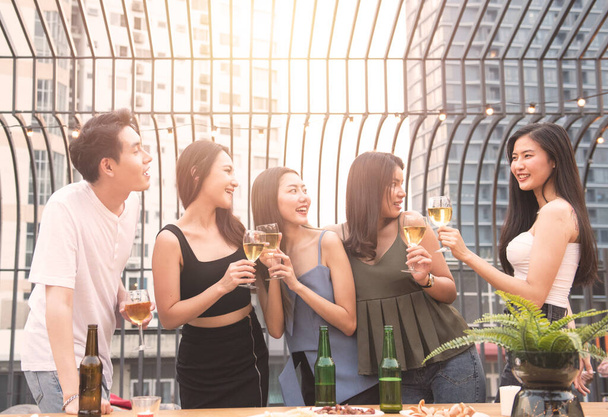 Group of asian multiple gender holding glass of wine chat together with friends while celebrating dance party on outdoor rooftop nightclub,leisure lifestyle of young friendship enjoyment concept. - Foto, imagen