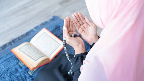 アジアの若い美しいイスラム教徒の女性の側ビーズで祈るとクルアーンを読むモスクで瞑想とカーペットマットの上に座る. - 写真・画像