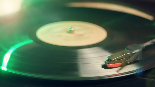 Retro record player with a spinning black vinyl record reflecting green light - Foto, Bild