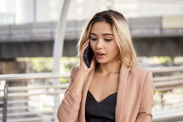 Attractive beautiful American businesswoman talking on smart phone to discuss business project in city. Smile happy woman with golden hair talking with curious or shock face. - Photo, image