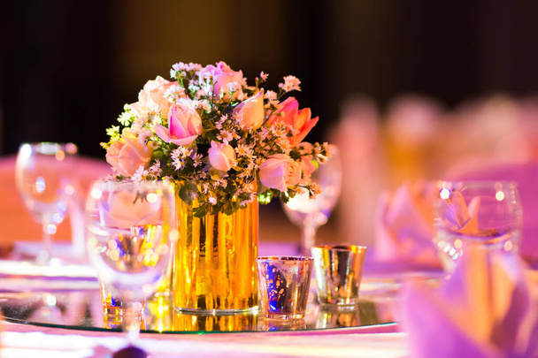 rose florist in glass vase decoration on dinner table with silverware and candle Indian wedding setup indoor with decorative lights and beautiful bokeh. - Photo, Image