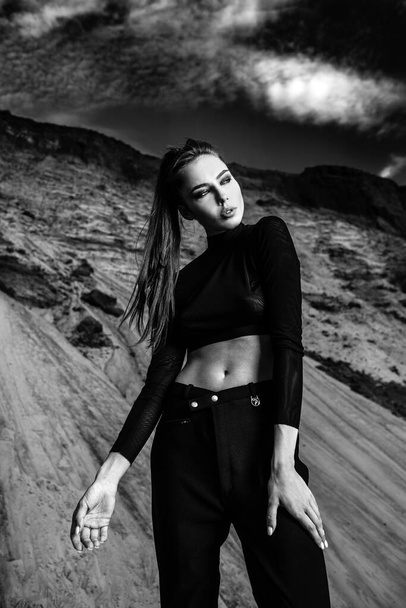 black and white shooting: a girl in a black top and trousers against the background of a mountain - Valokuva, kuva