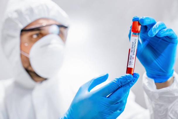 Άνδρας γιατρός επιστήμονας κρατώντας δοκιμαστικό σωλήνα με δείγμα αίματος για την έρευνα του κορωναϊού στο κλινικό εργαστήριο - Φωτογραφία, εικόνα