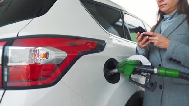 Woman using smartphone while her car is refueling. Slow motion - Footage, Video