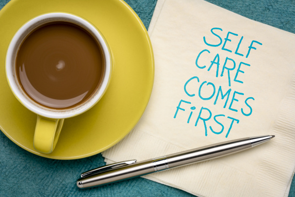 zelfzorg komt op de eerste plaats inspirerende herinnering - handschrift op een servet met koffie, lichaam positief, geestelijke gezondheid slogan - Foto, afbeelding