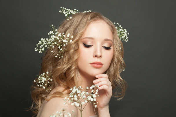 Nice blonde woman with long healthy curly hair and white flowers. Attractive girl with makeup and wavy hairstyle on dark background - Fotografie, Obrázek