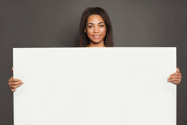 Mujer negra sosteniendo una gran pancarta blanca vacía cantando sobre fondo gris de pancarta
 - Foto, imagen