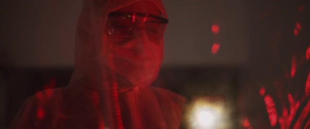 Mann im Schutzanzug mit Maske und Brille, ein Foto mit dem Handy, hinter einer PVC-Folie. Gesundheitskonzept, Virenschutz, Pandemie. Rotlicht, Zeitlupe. BMPCC 4K - Filmmaterial, Video