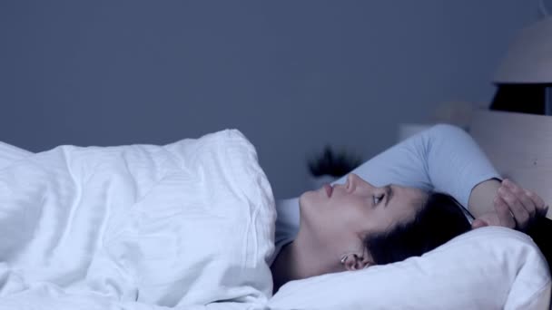 Girl can not fall asleep. Insomnia noisy neighbors concept. Young attractive caucasian girl lies alone in bed under covers and looks at ceiling. Medium shot - Footage, Video