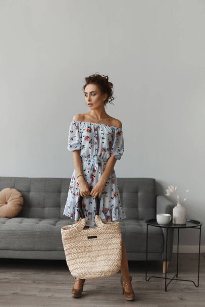 Young beautiful woman with perfect body in a short dress posing in the interior. Model girl with curly hair in light spring dress posing with a trendy bag. Spring fashion. Summertime lifestyle - Photo, image
