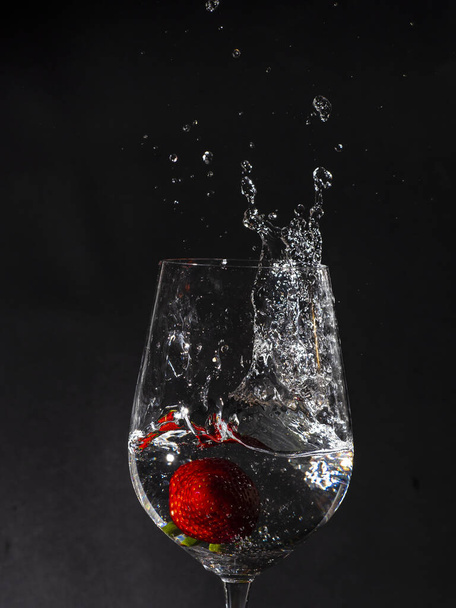 Imagem de fundo preto de um copo com água caindo um movimento de morango e água gelada com um monte de espirrar
 - Foto, Imagem