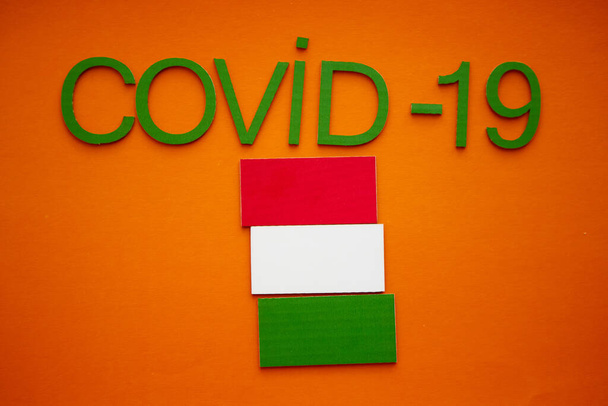 Hongaarse vlag en Word COVID-19 gemaakt van groene kartonnen letters, geïsoleerd op oranje achtergrond. Wereldgezondheidsorganisatie WHO introduceerde nieuwe officiële naam voor Coronavirus genaamd COVID-19. - Foto, afbeelding