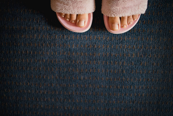 濃い青のカーペットの背景にピンクのふわふわのスリッパを着た女性の足。コピースペース,平らなレイアウト,ミニマリズム. - 写真・画像