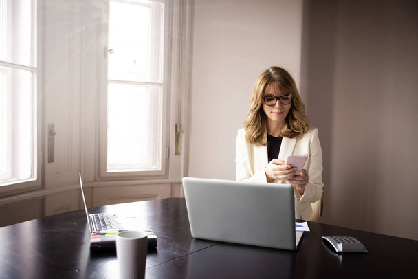 Φωτογραφία της ελκυστική γυναίκα κάθεται στο γραφείο πίσω από το laptop της και γραπτών μηνυμάτων, ενώ εργάζονται από το σπίτι. - Φωτογραφία, εικόνα