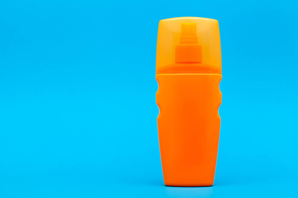 orange unlable bottle of sunscreen on a blue background with copy space. - Фото, изображение