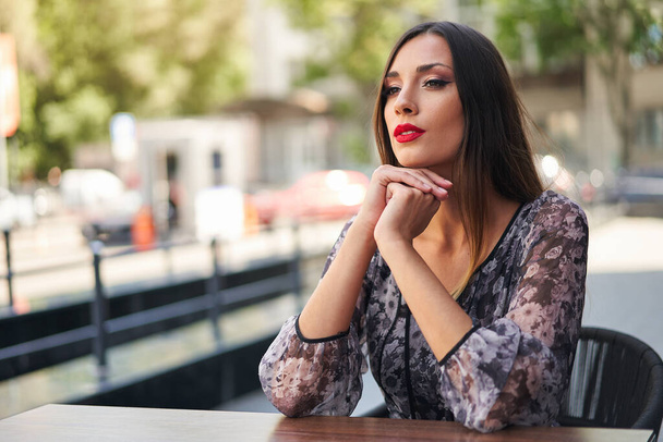 Beautiful elegant young girl with dark dyed long hair sits at a table summer outdoor cafe waiting for her boyfriend. European woman resting after shopping. Free space for text - Valokuva, kuva