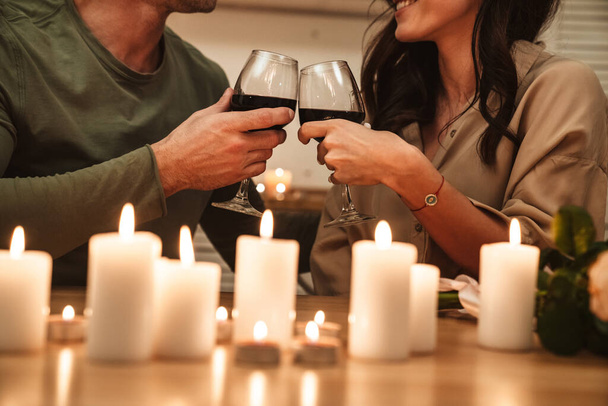 Image of happy passionate couple drinking red wine from glasses while having romantic candlelight dinner at home - Foto, immagini