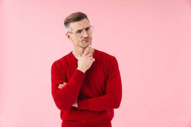Portrait of handsome caucasian man wearing eyeglasses frowning and thinking isolated over pink background - Фото, изображение