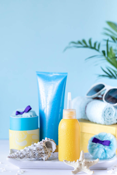 Zonnecrème flessen, glazen, zeesterren palmbladeren op een blauwe achtergrond. Schoonheid en zorg in de zomer. - Foto, afbeelding