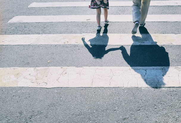 Pavimento strutturato sfondo con gambe e ombre cittadini attraversando strada asfaltata a zebra passerella
 - Foto, immagini