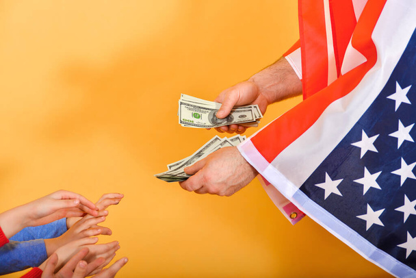 Amerikan lipun alla olevan miehen käsi ojentaa rahaa lasten käsiin, käsite riippuvuudesta Yhdysvalloista
. - Valokuva, kuva