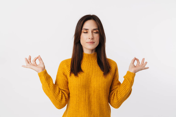 Image of beautiful brunette adult woman wearing sweater keeping fingers together for meditation isolated over white background - Φωτογραφία, εικόνα