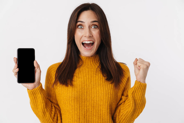 Image of beautiful brunette adult woman wearing sweater screaming and holding cellphone isolated over white background - Photo, image