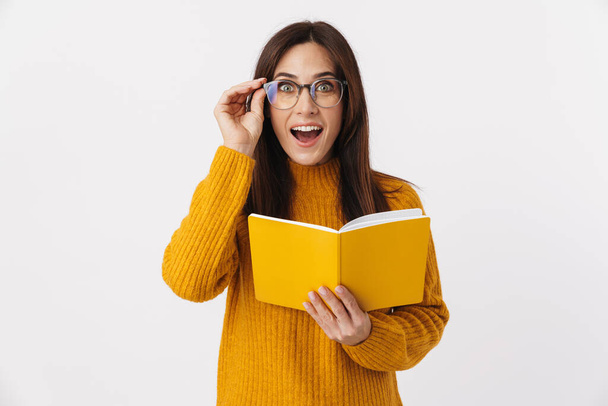 Image of beautiful brunette adult woman wearing eyeglasses making notes in diary book isolated over white background - Φωτογραφία, εικόνα