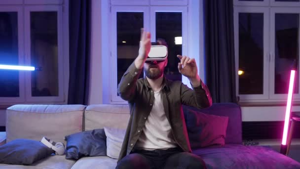 Handsome concentrated bearded young man in special 3d glasses scrolling virtual display ,sitting in the violet light room - Video