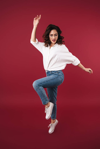 Photo of a pretty beautiful young woman jumping isolated over red wall background. - Foto, immagini