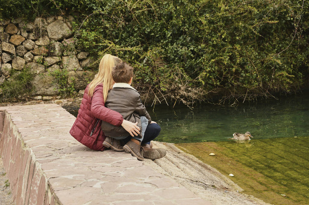 Madre e hijo observando la balsa de agua con patos. Colores de la naturaleza
 - Foto, Imagen
