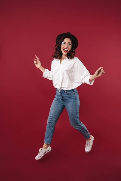 Picture of a pretty positive young woman jumping isolated over red wall background. - 写真・画像
