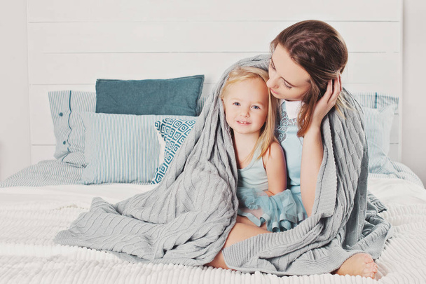 Porträt einer glücklichen Familie zu Hause. Niedliche Mutter und kleine Tochter mit Baumwolle karierte Decke - Foto, Bild
