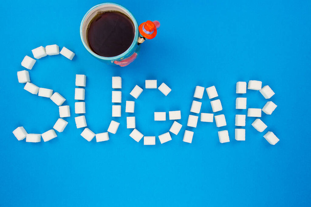 Sugar cubes and two cups on an isolated blue background making up a word sugar. Pink and blue cups with white cubes of sugar isolated on blue background. Concept word sugar. Flat lay background. - Φωτογραφία, εικόνα