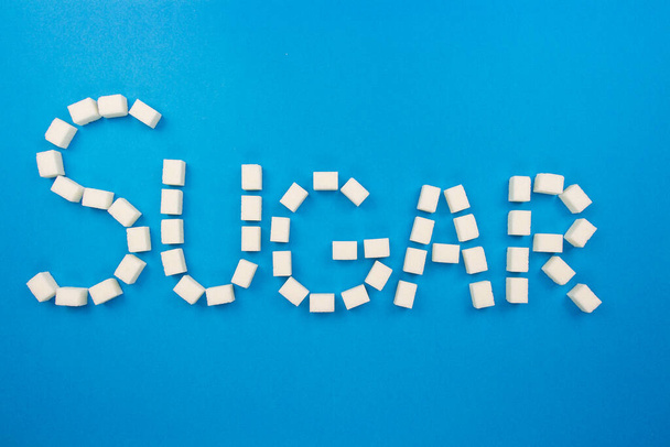 Sugar cubes on an isolated blue background making up a word Sugar. White cubes of sugar isolated on blue background. Concept word sugar made up of cubes of sugar. Flat lay background. - Foto, imagen