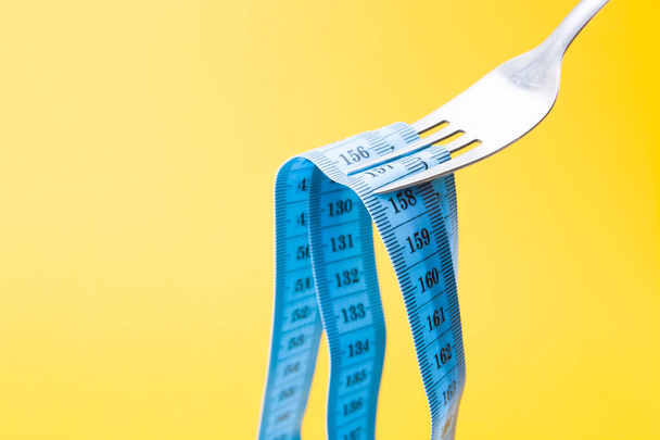 niebieska taśma pomiarowa na widelcu jak pasta na żółtym tle koncepcja diety na czczo odchudzanie i odchudzanie - Zdjęcie, obraz